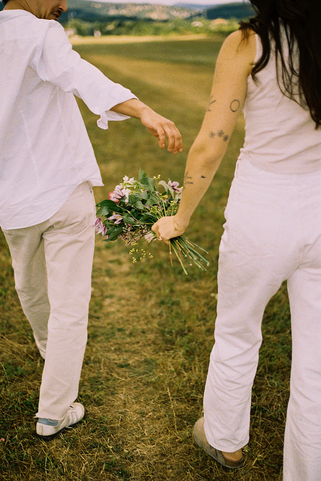 A couple dressed in white embraces outdoors, with greenery in the background during their candid engagement photos