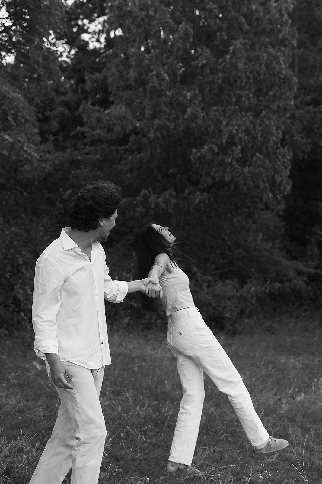 A couple in matching white outfits laughs together outdoors.