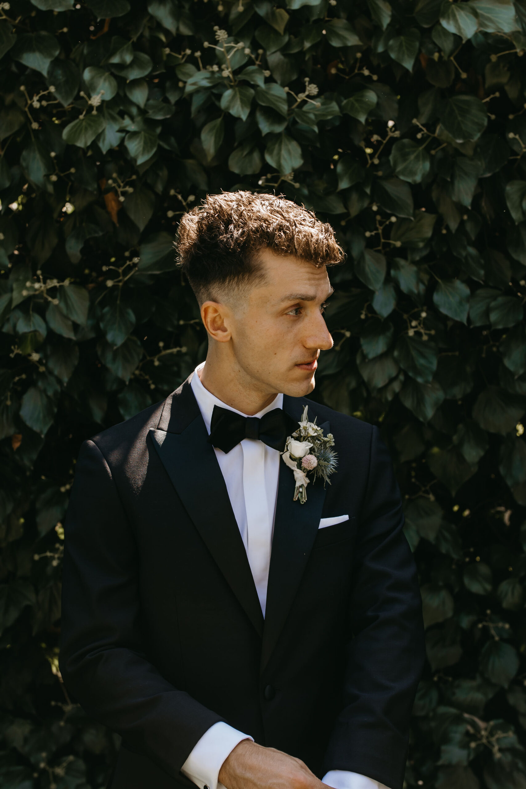 Groom standing outdoors in front of a green background | documentary style wedding photos