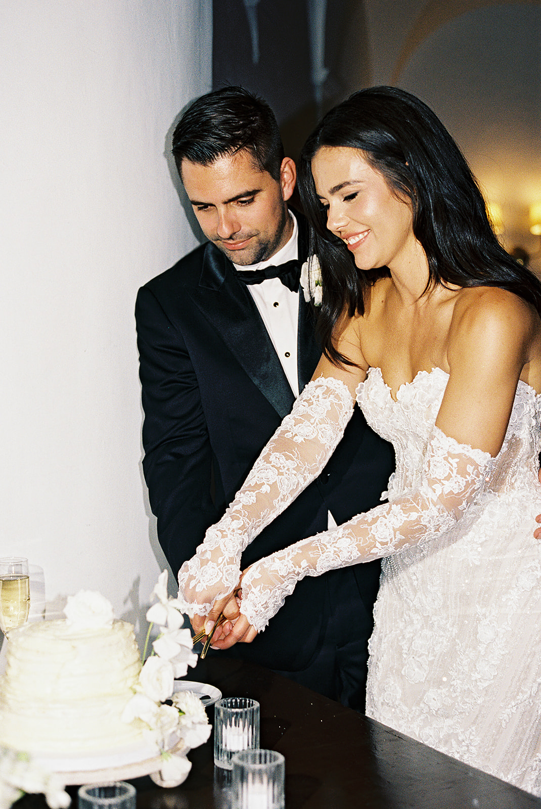 Bride and groom in formal attire cutting a white wedding cake together.