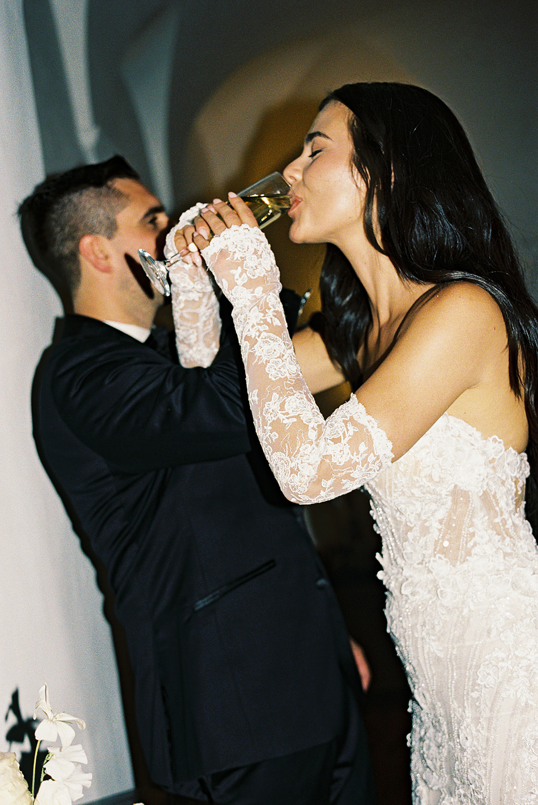 Bride and groom in formal attire cutting a white wedding cake together.