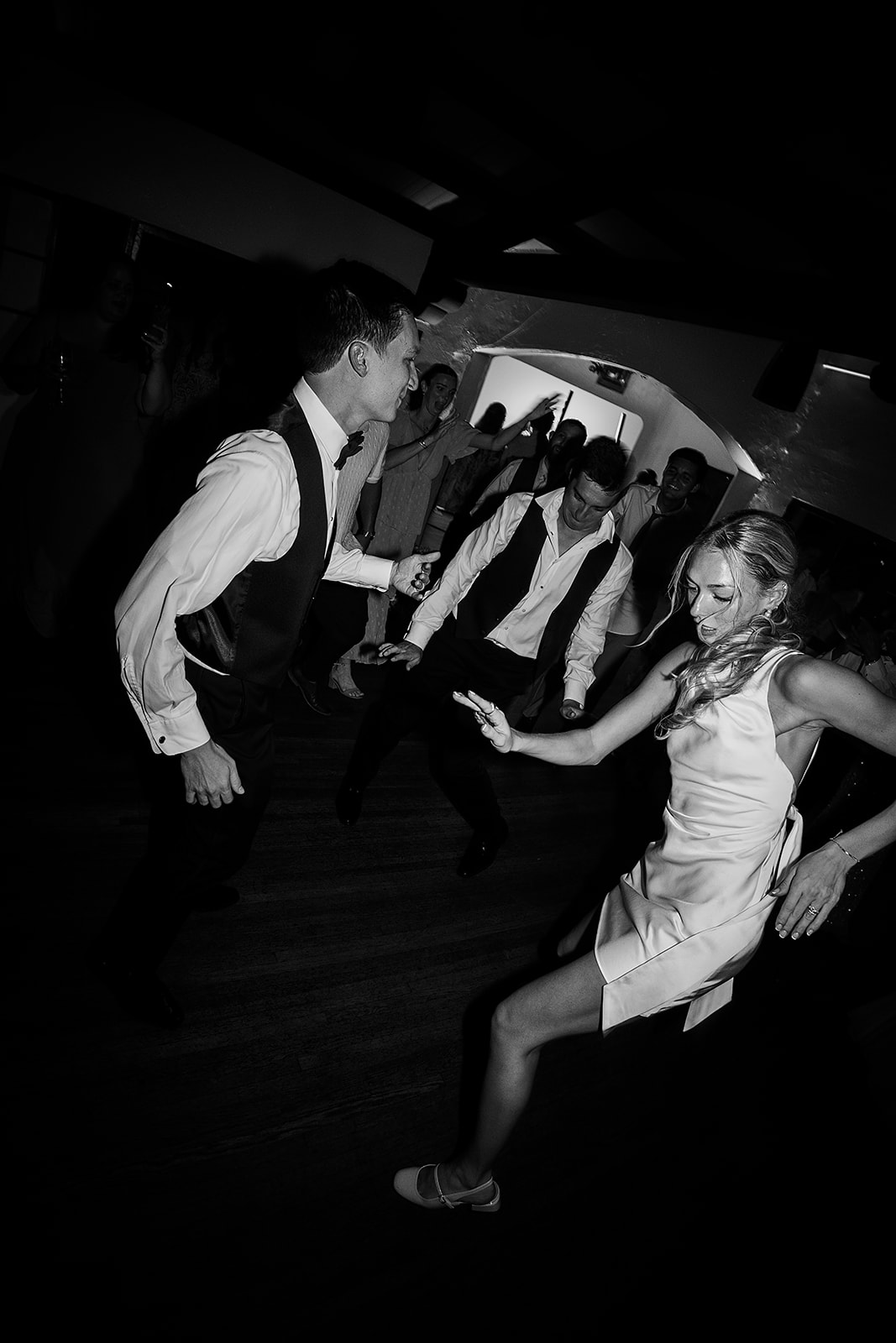 People dancing energetically at a party, wearing formal attire, in a black and white photograph.