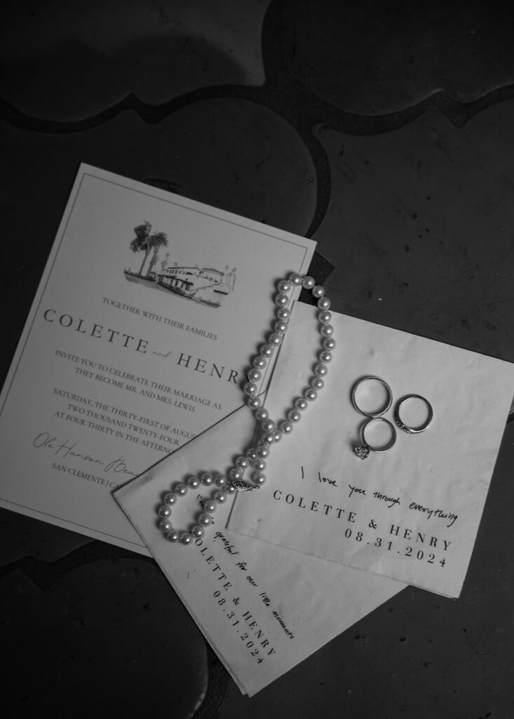 A pearl necklace and two rings rest on wedding invitation cards with the names Colette and Henri. The date on the cards is September 9, 2023.