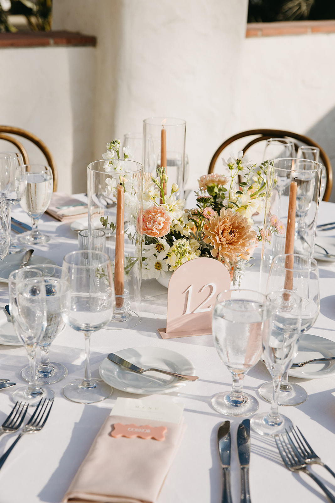 A table set for a wedding reception with floral centerpieces, tapered candles, and a table number 12. White tablecloth, glassware, and cutlery are neatly arranged at Ole Hanson