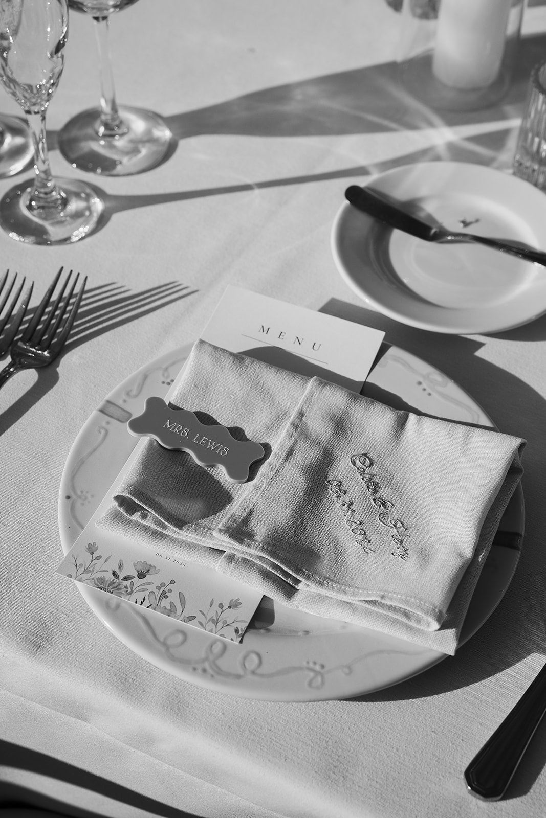 Black and white image of a table setting with a plate, folded napkin, cutlery, glasses