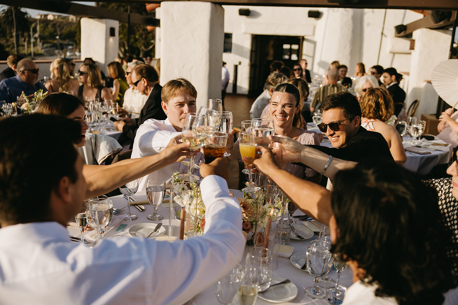 A group of people sitting at an outdoor event table raise their glasses in a toast.