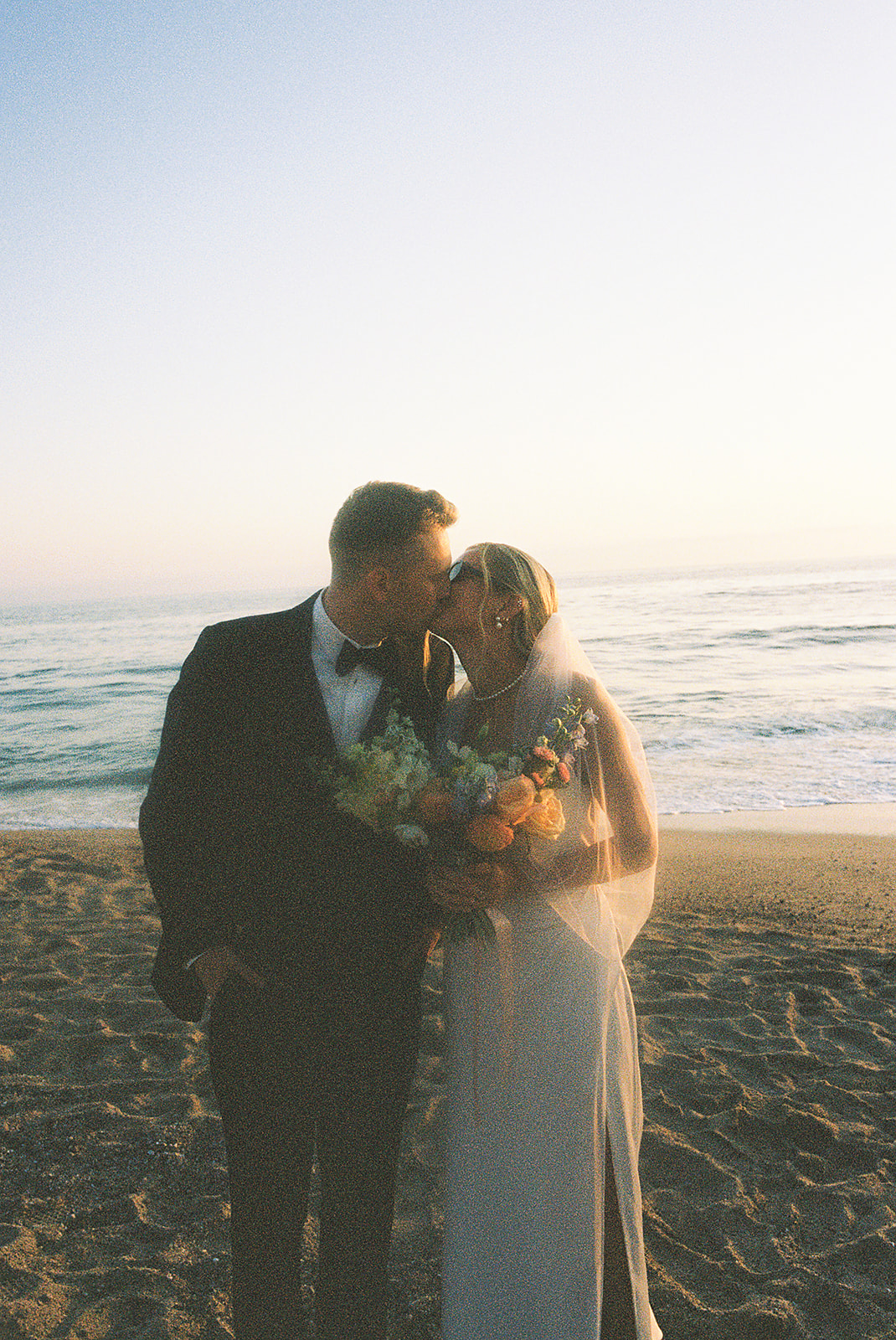 A bride and groom embrace and smile at each other against a soft, blurred background.