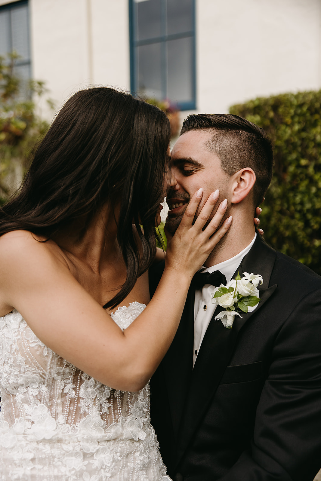 A couple in formal attire share an intimate moment. The woman is in a white dress and the man wears a tuxedo with a floral boutonniere.