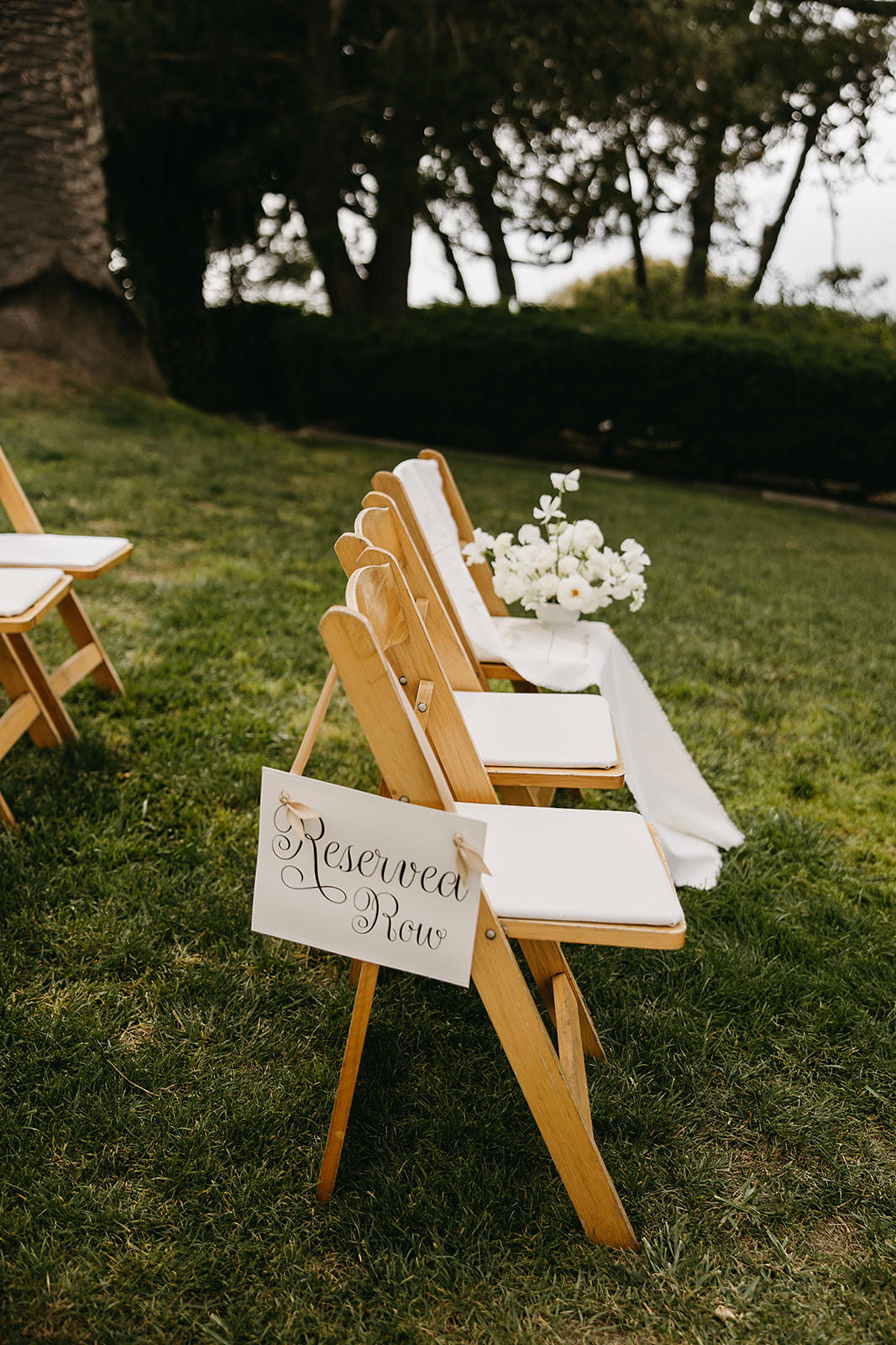 An outdoor wedding ceremony setup with wooden chairs arranged in rows facing an altar adorned with white flowers, overlooking a scenic ocean view under a clear sky at La Venta Inn