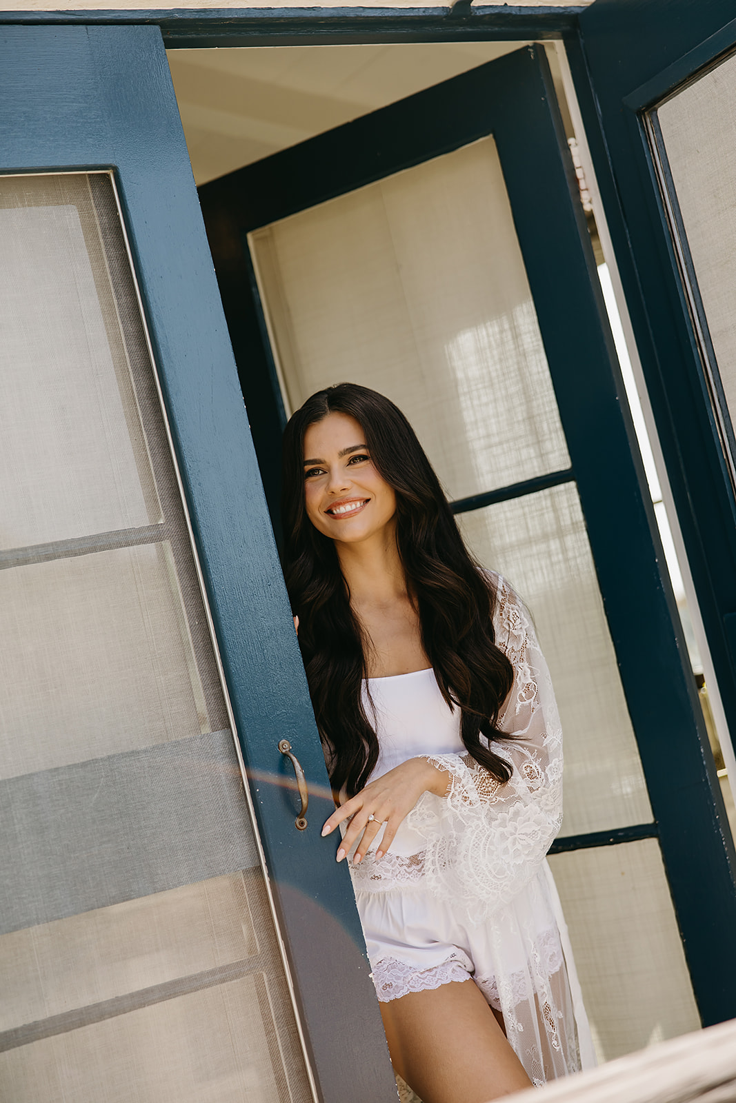 Woman in a lace robe sprays perfume while looking at her reflection in a decorative mirror, getting ready for her wedding at La venta inn