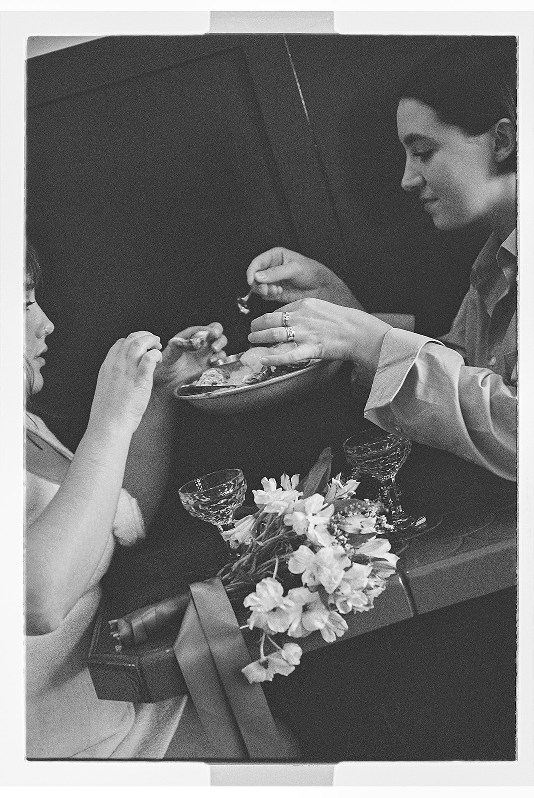 Two people clink glasses in a toast at a table, with a bouquet of white flowers and a dish in the background.