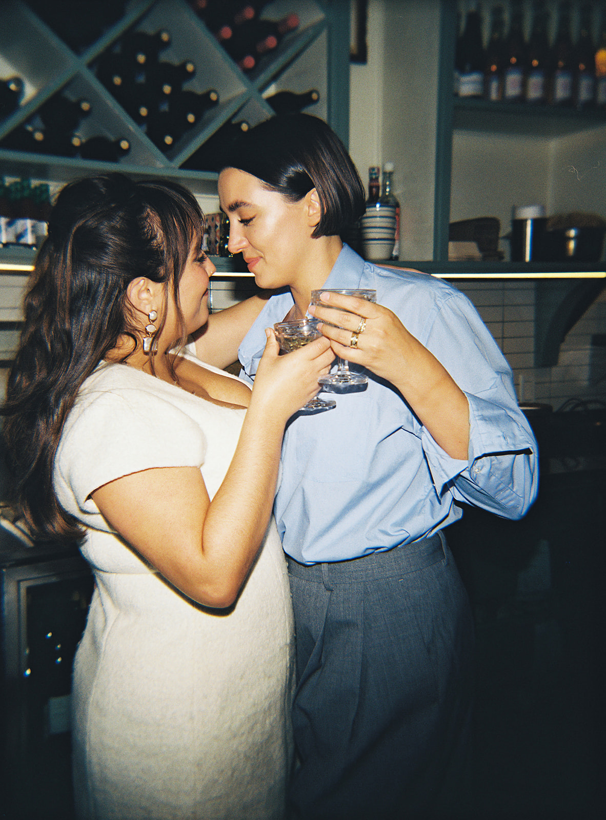 Two people smiling closely, holding drinks, in a cozy bar setting.