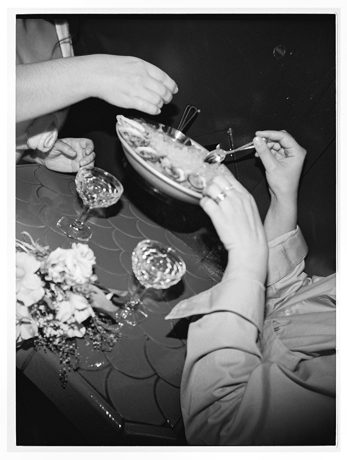 Two people clink glasses in a toast at a table, with a bouquet of white flowers and a dish in the background.