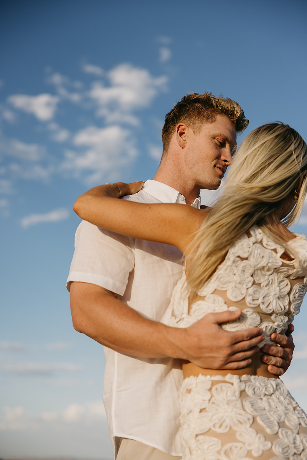 A couple holding hands walks through a desert landscape under a clear blue sky for their joshua tree engagement photos