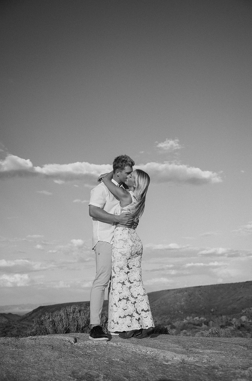 A couple holding hands walks through a desert landscape under a clear blue sky for their joshua tree engagement photos