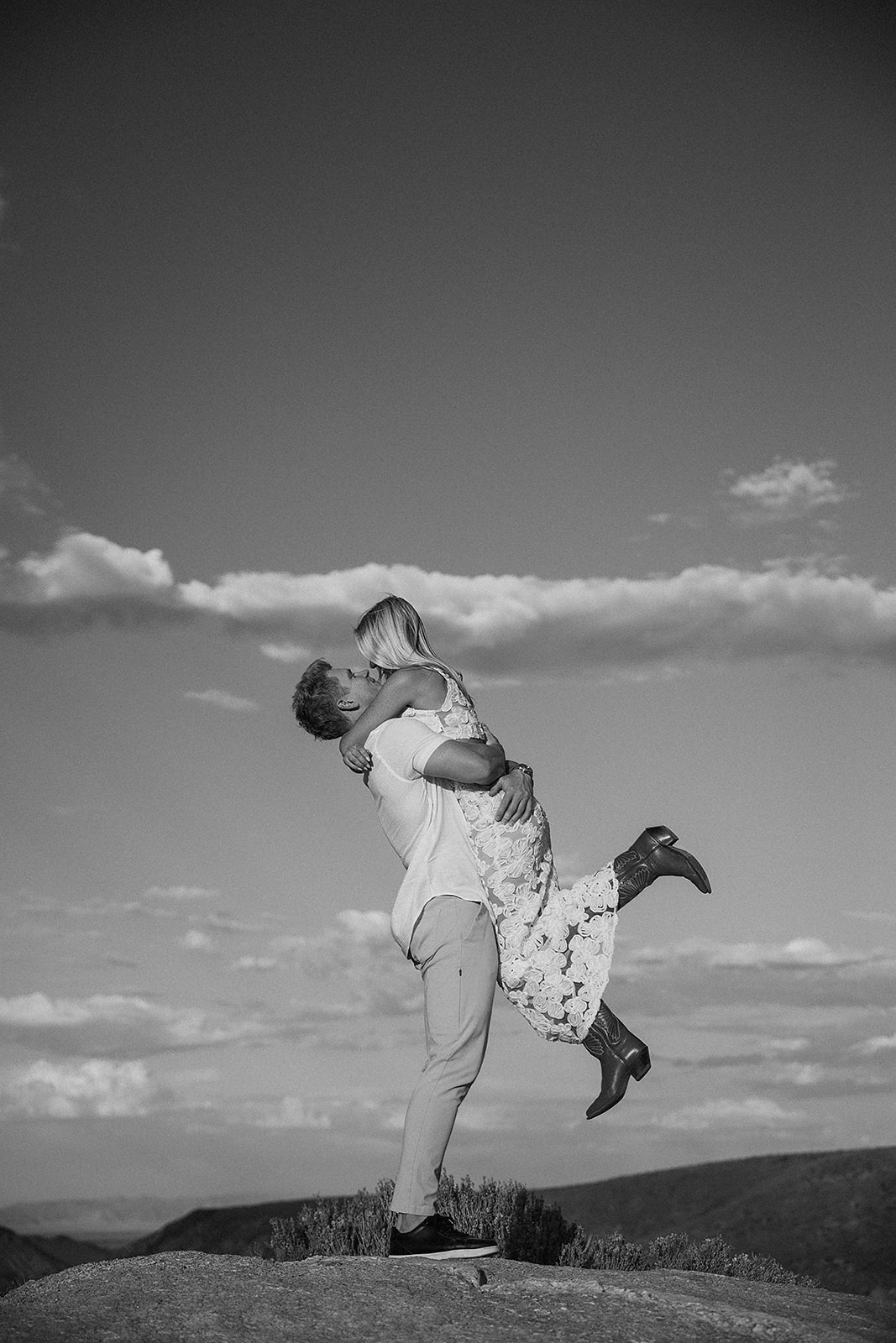 A couple holding hands walks through a desert landscape under a clear blue sky for their joshua tree engagement photos