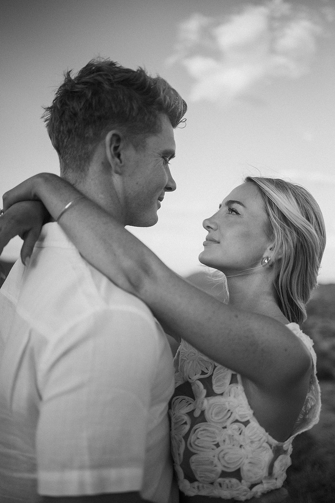 A couple holding hands walks through a desert landscape under a clear blue sky for their joshua tree engagement photos