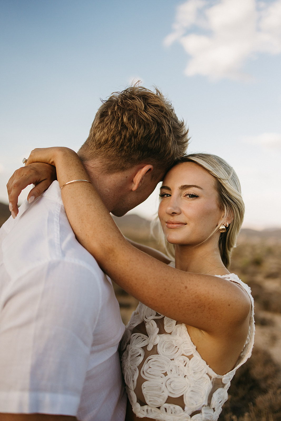 A couple holding hands walks through a desert landscape under a clear blue sky for their joshua tree engagement photos