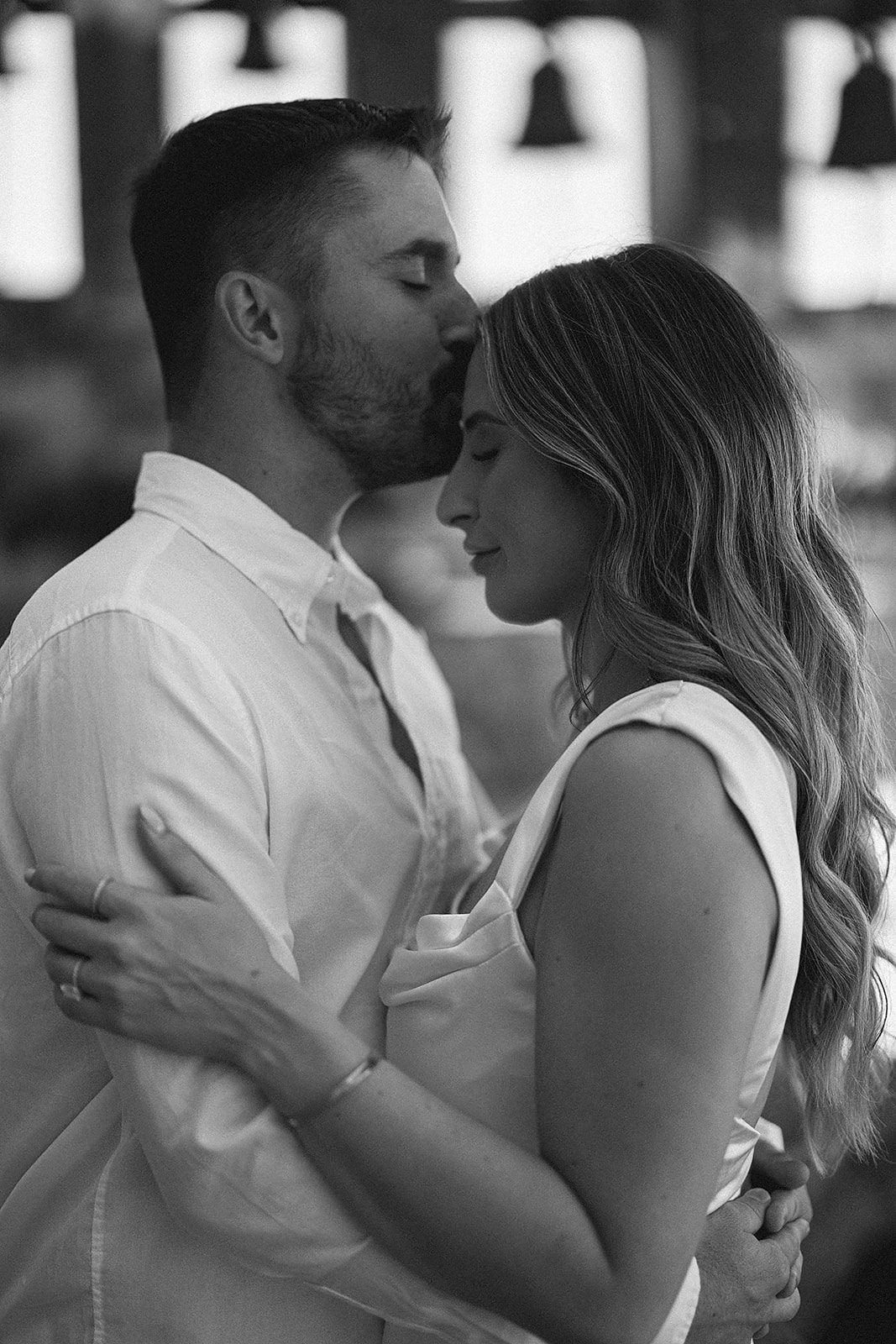 A couple embraces closely, with the man's forehead resting on the woman's head, both appearing peaceful and content. The image is in black and white.