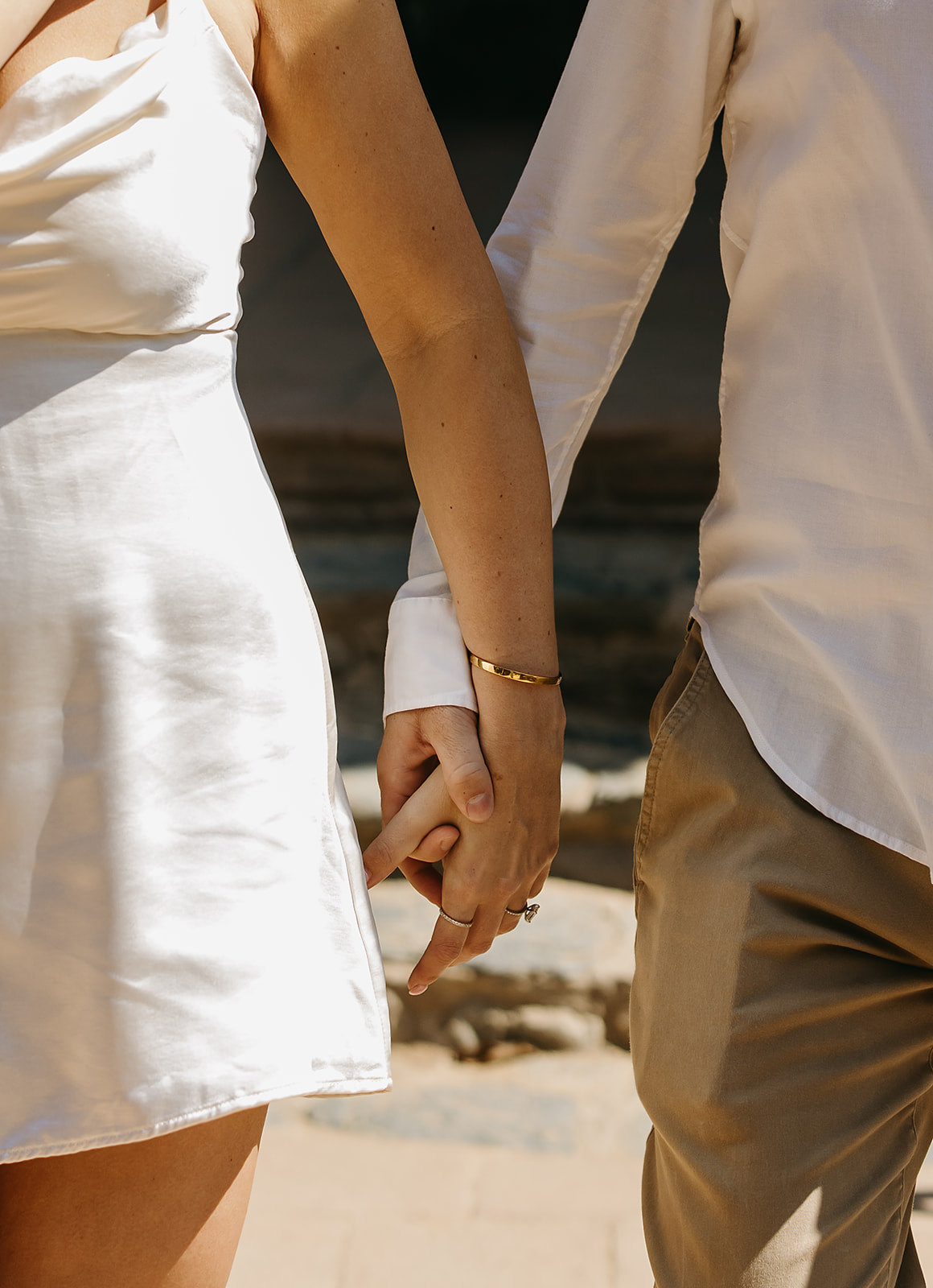 A couple stands close and embraces on a sunlit patio, with steps and a dark doorway in the background for their candid engagement photography 