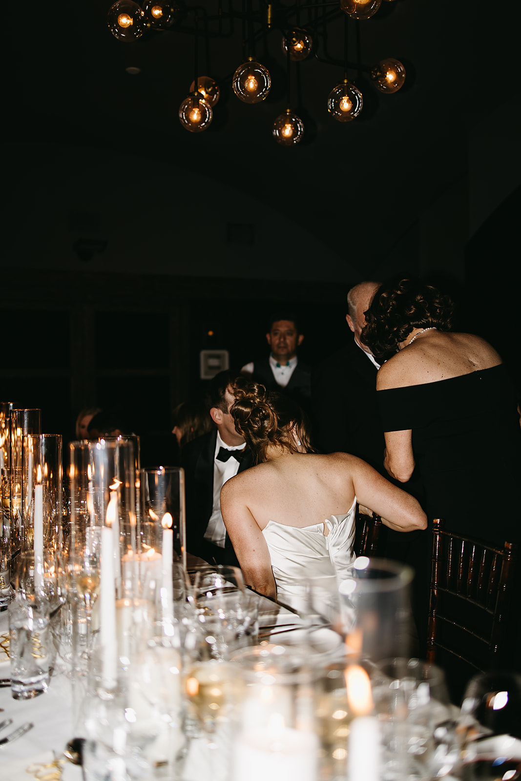 A formal dinner setting with guests seated at a table adorned with lit candles and glassware.