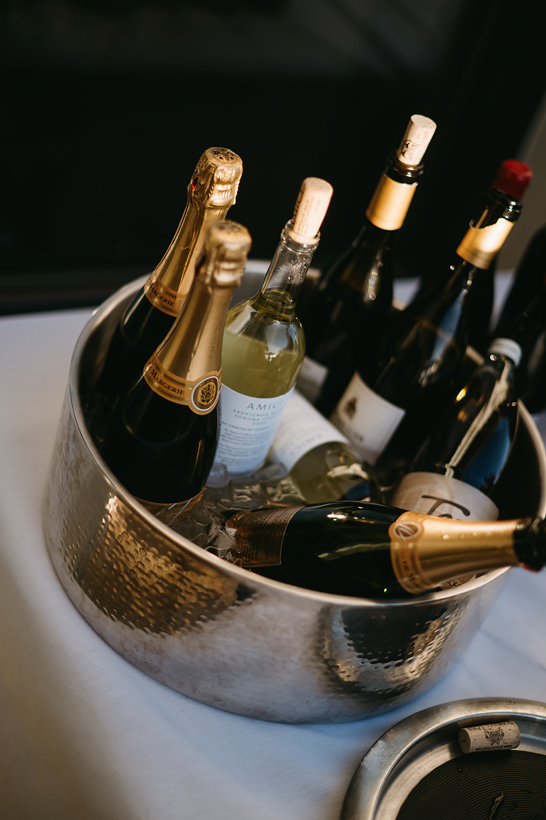 A silver ice bucket filled with various bottles of wine and champagne, set on a white tablecloth.