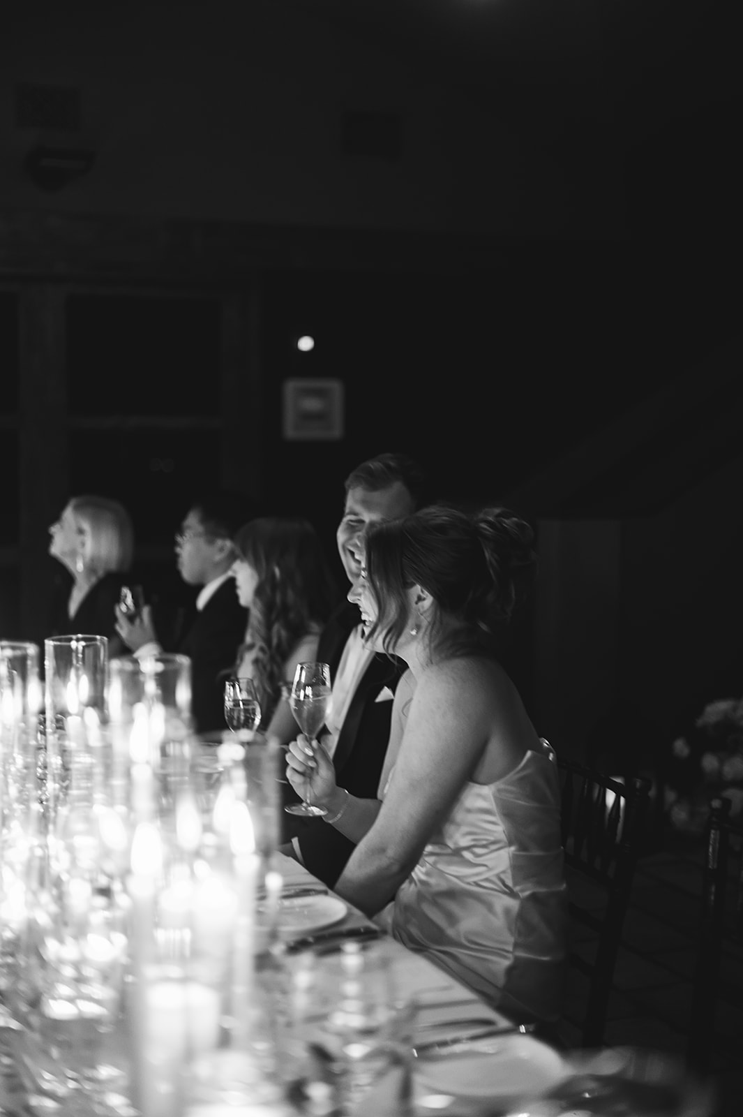 A group of people seated at a long table with lit candles, dressed formally, in a dimly lit setting.