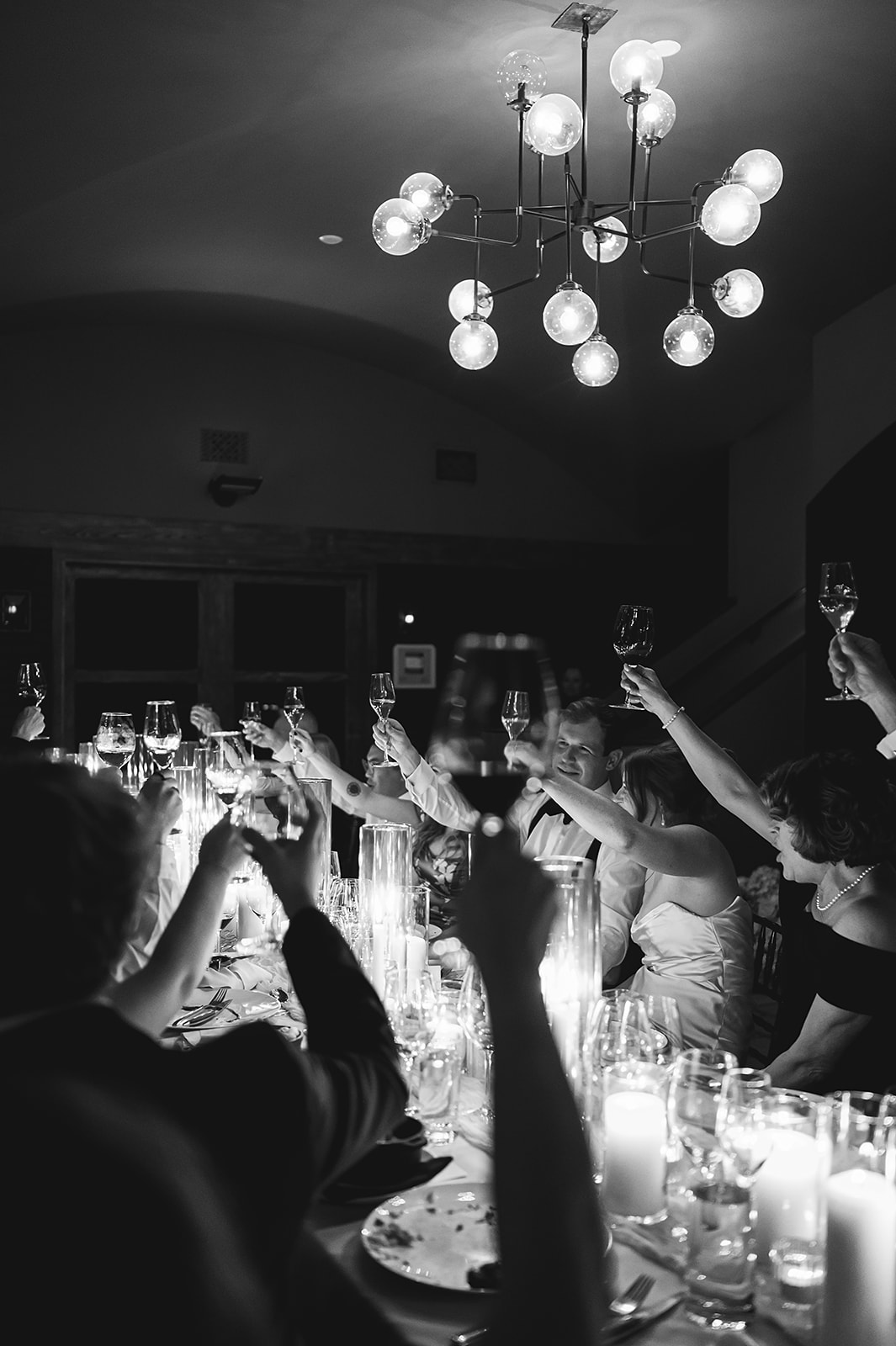 A group of people seated at a long table with lit candles, dressed formally, in a dimly lit setting.