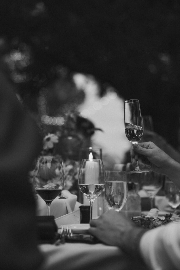 People holding glasses around a candlelit table, with flowers and plates visible, in an outdoor setting at quail ranch