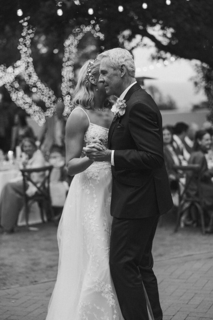 A couple dances together at an outdoor event. The scene is in black and white, with lights and guests visible in the background st quail ranch