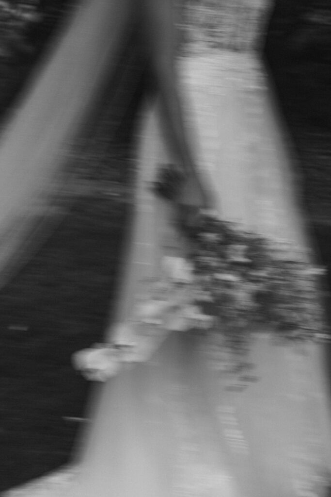 Blurry black and white photo of a person in a long dress holding a bouquet.