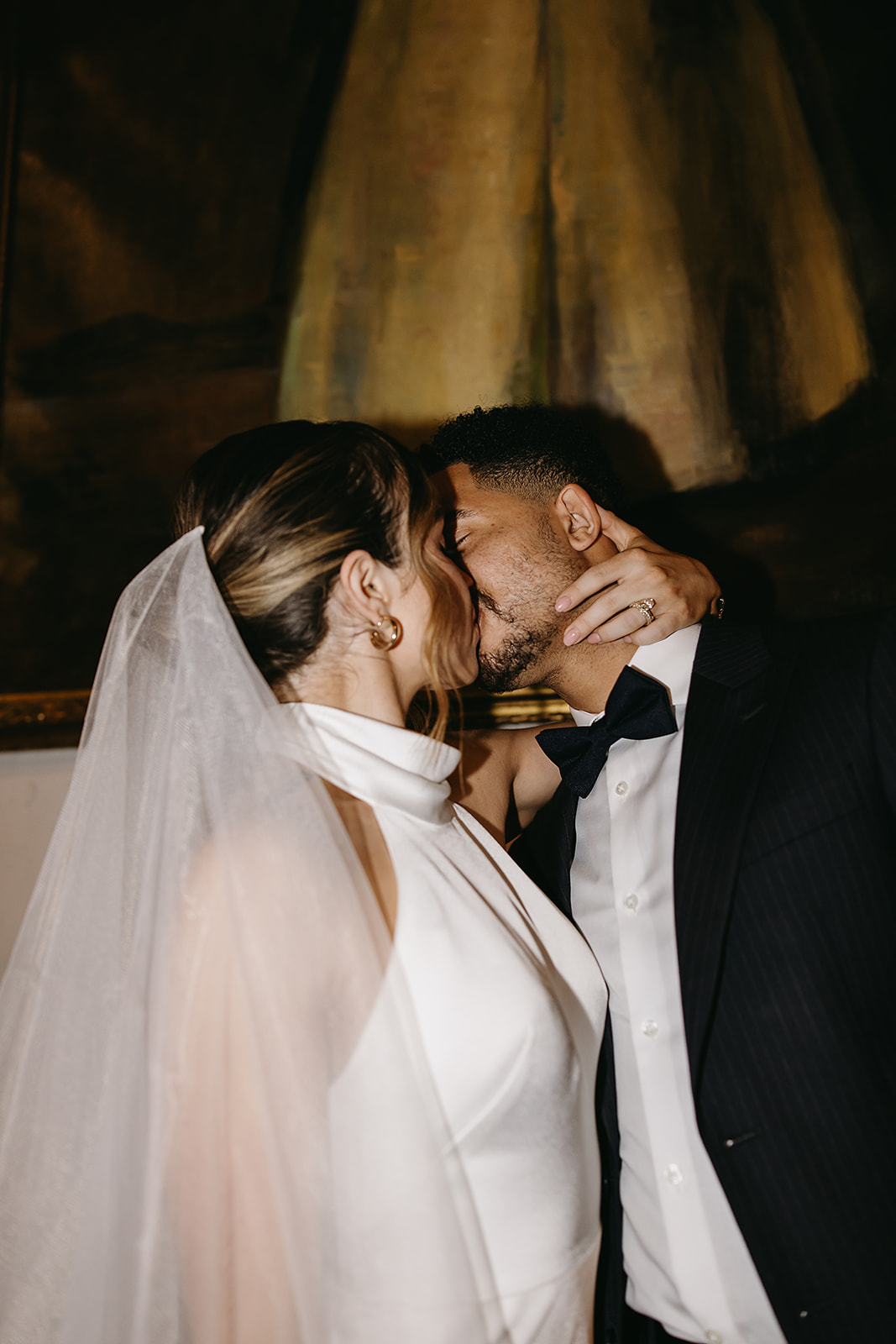 A bride and groom share a kiss. The bride is wearing a white dress and veil, and the groom is in a black suit. They are standing indoors for their santa barbara elopement