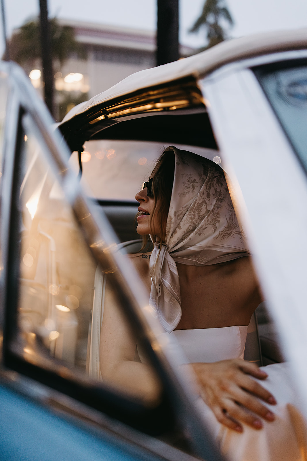 Person in a white dress and scarf sits in the backseat of a car, looking out the window at a santa barbara elopment.