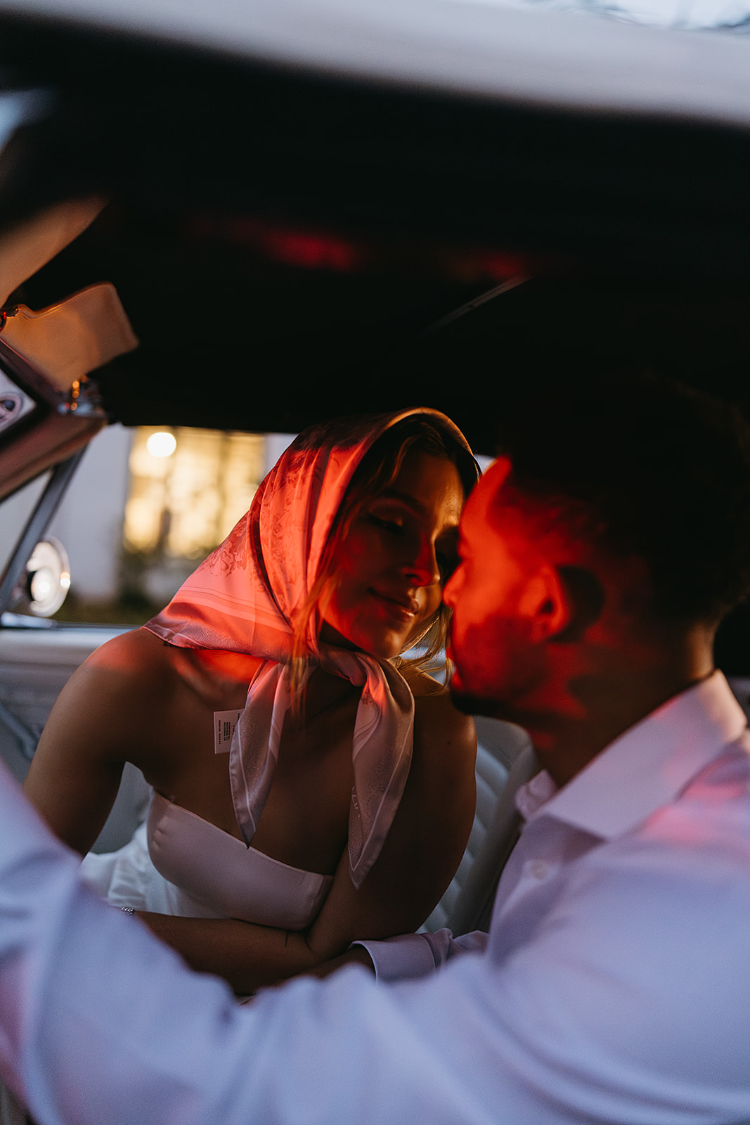 Bride and groom sit in a vintage convertible, the bride holding a bouquet. The lighting is dim, casting a warm glow inside the car for their santa barbara elopment