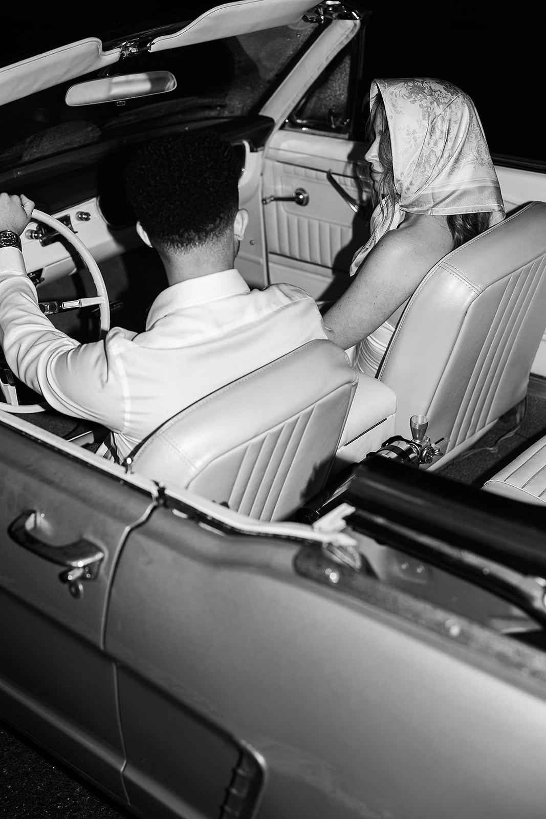 Bride and groom sit in a vintage convertible, the bride holding a bouquet. The lighting is dim, casting a warm glow inside the car for their santa barbara elopment