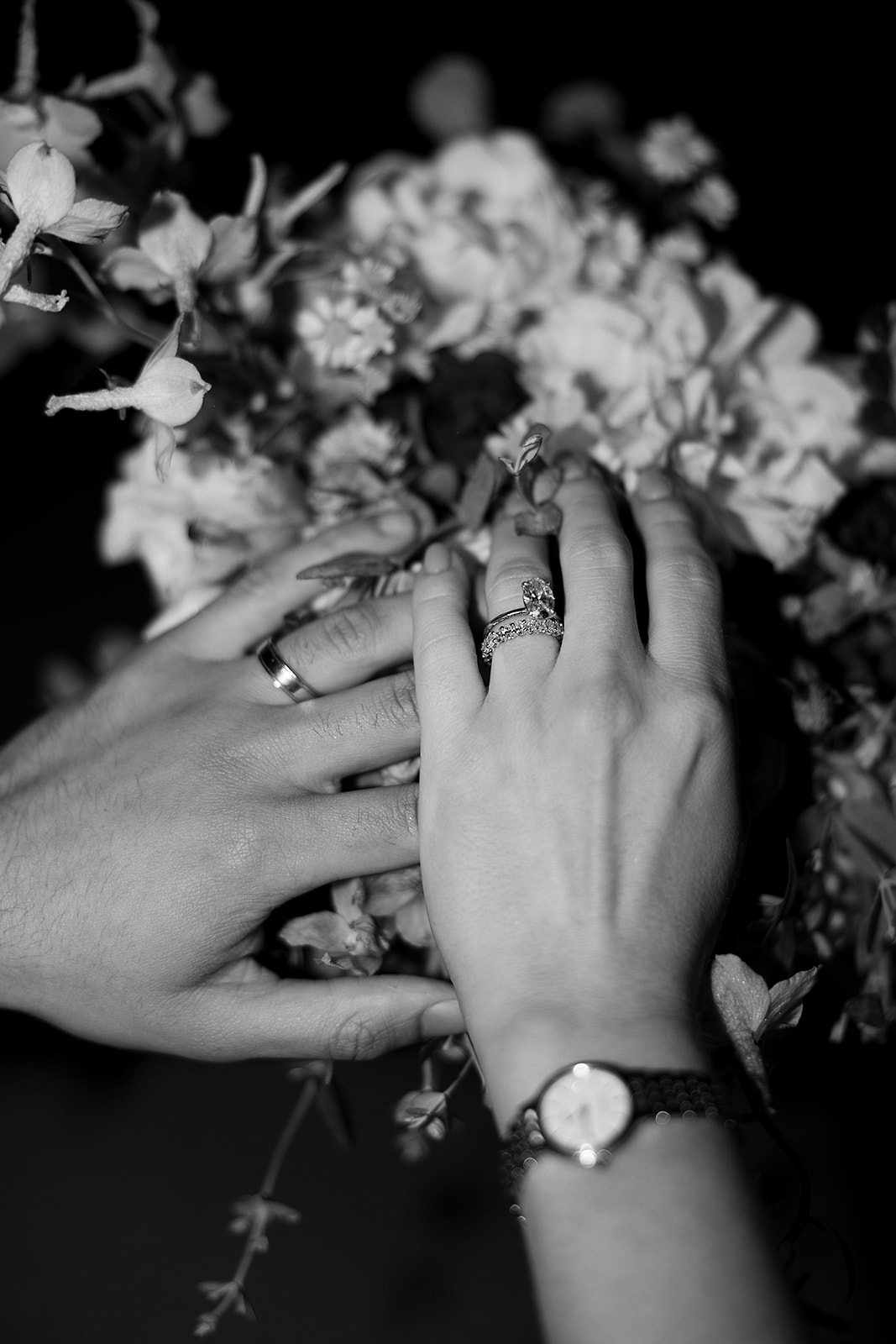 Hands with rings touching a bouquet of flowers. Black and white image.