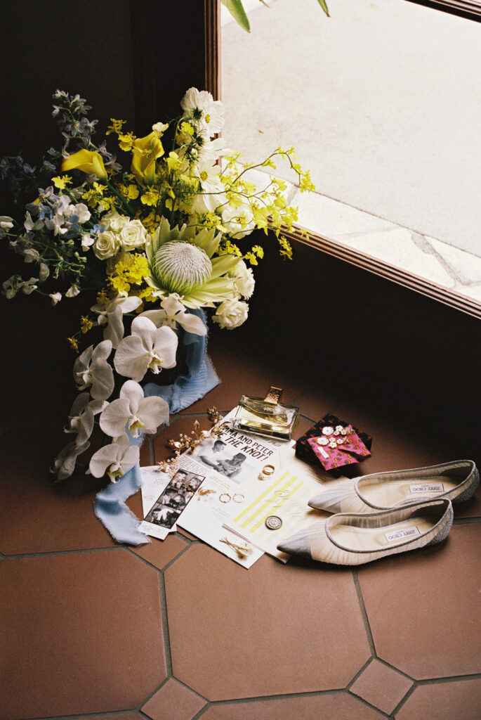 Bouquet of flowers, white shoes, and various small items are arranged on a tiled floor near a window.