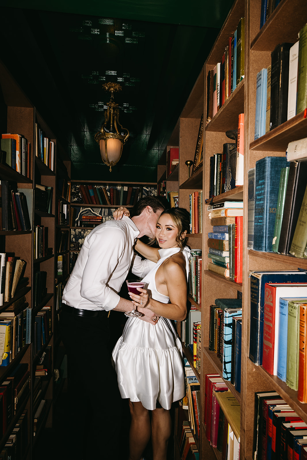 A couple in formal attire shares a dance in a restaurant with white tablecloths and dim lighting.