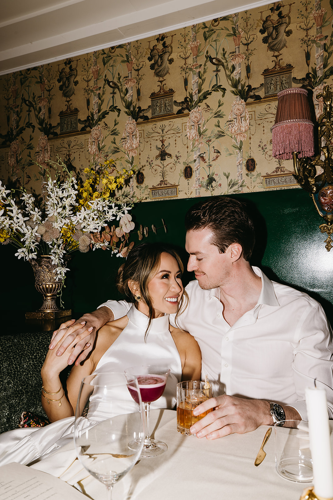 A couple in formal attire shares a dance in a restaurant with white tablecloths and dim lighting.