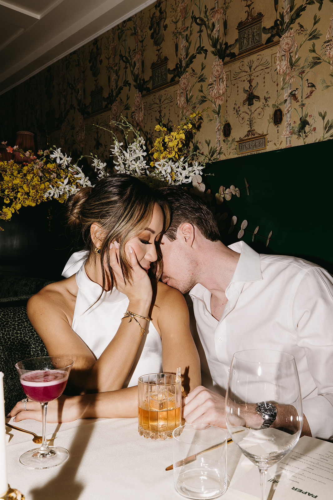 A couple in formal attire shares a dance in a restaurant with white tablecloths and dim lighting.