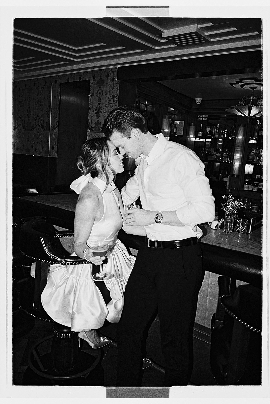 A couple in formal attire shares a dance in a restaurant with white tablecloths and dim lighting.