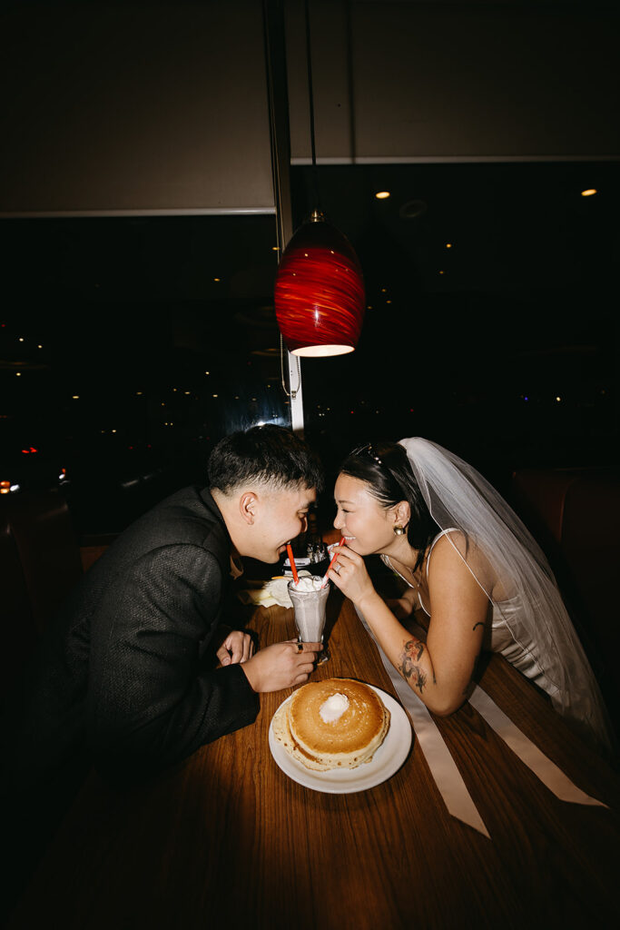 Two people sitting across from each other in a restaurant booth, wearing formal attire and sunglasses, under a red hanging light.