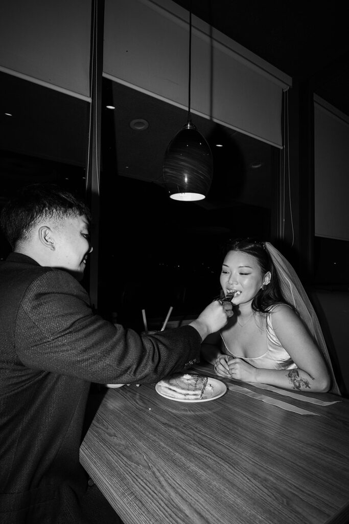 Two people sitting across from each other in a restaurant booth, wearing formal attire and sunglasses, under a red hanging light.