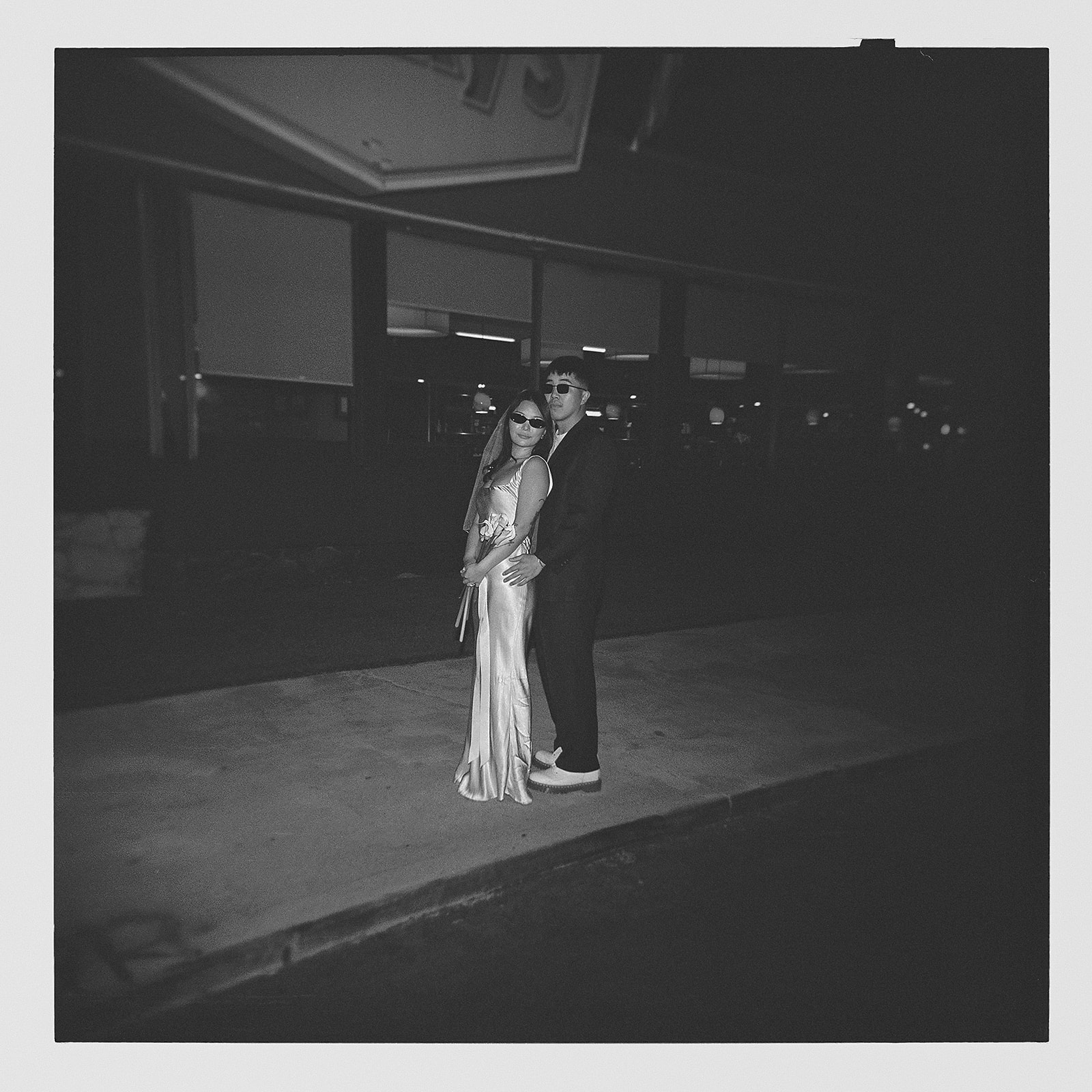 A couple stands outside a Denny's restaurant at night, dressed in formal attire.