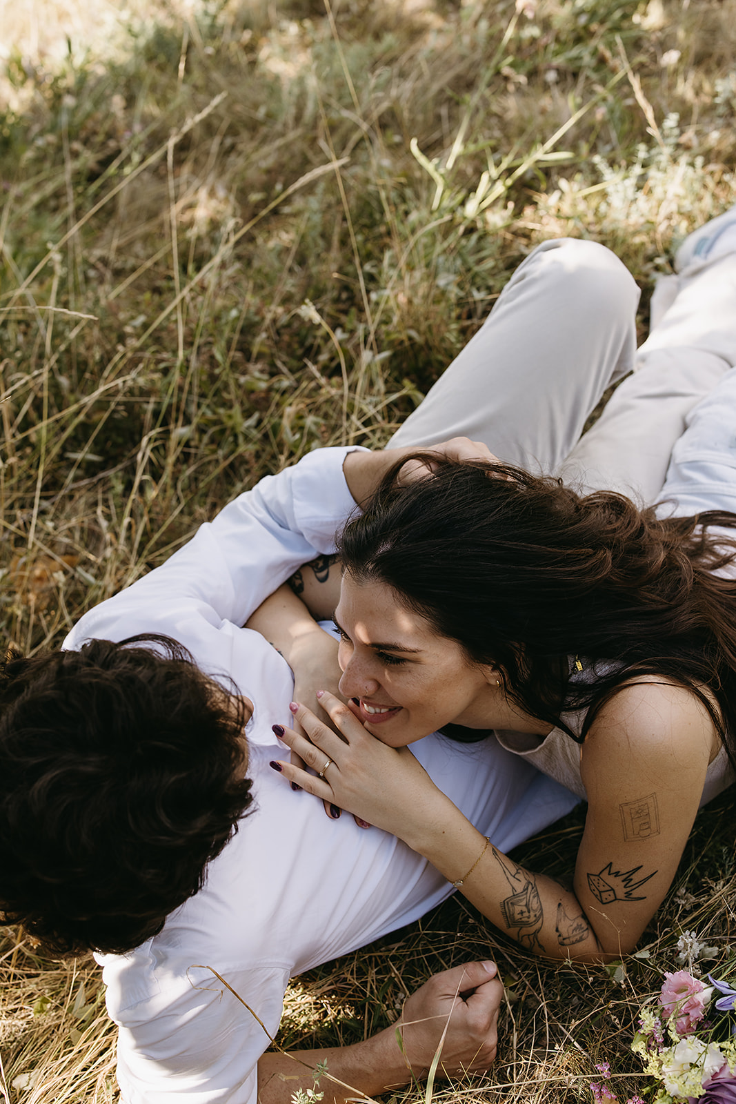 A couple dressed in white embraces outdoors, with greenery in the background during their candid engagement photos