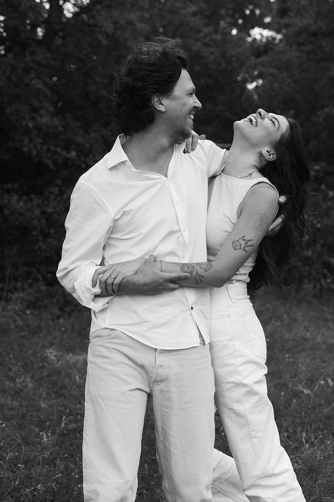 A couple in matching white outfits laughs together outdoors.