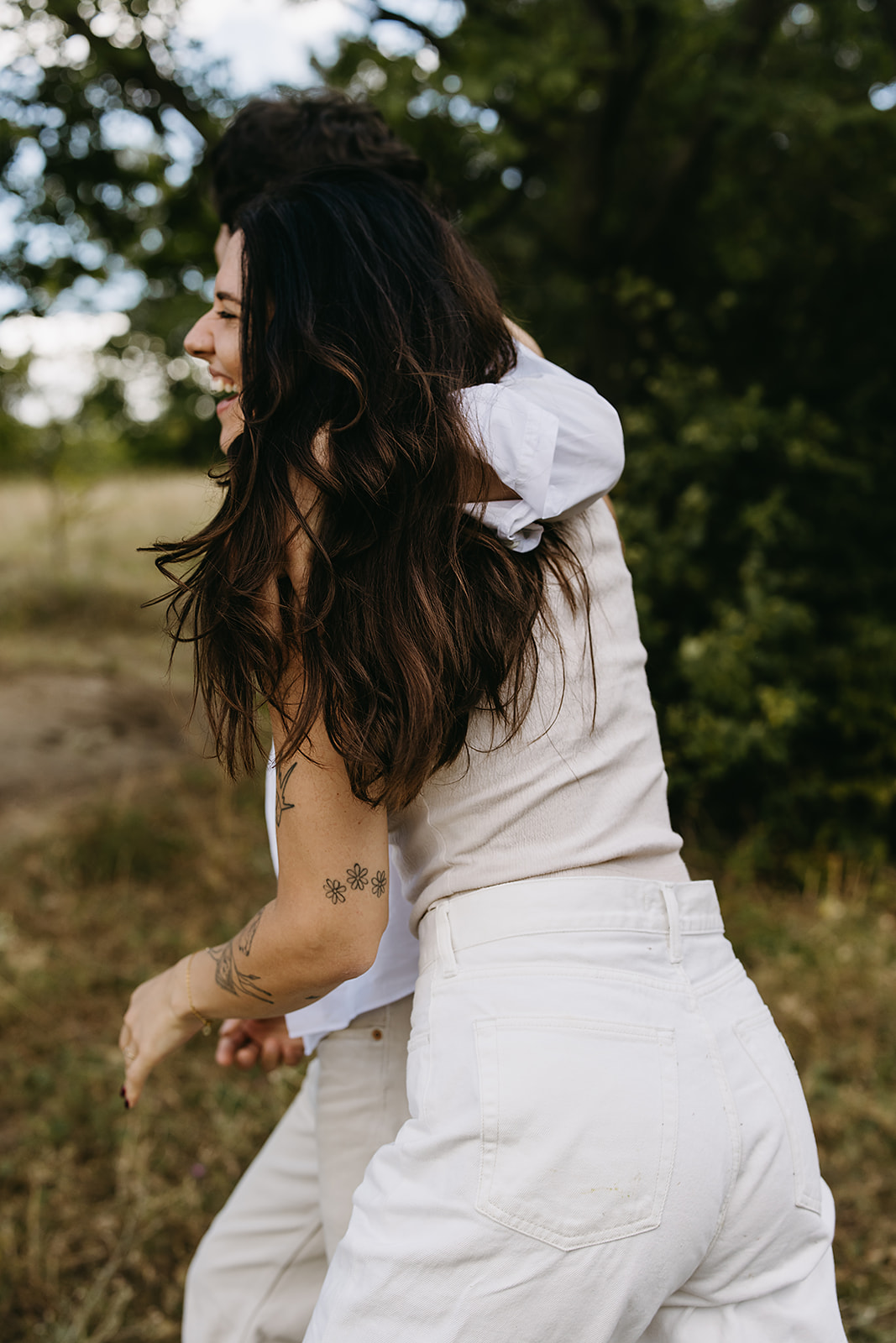 A couple in matching white outfits laughs together outdoors.