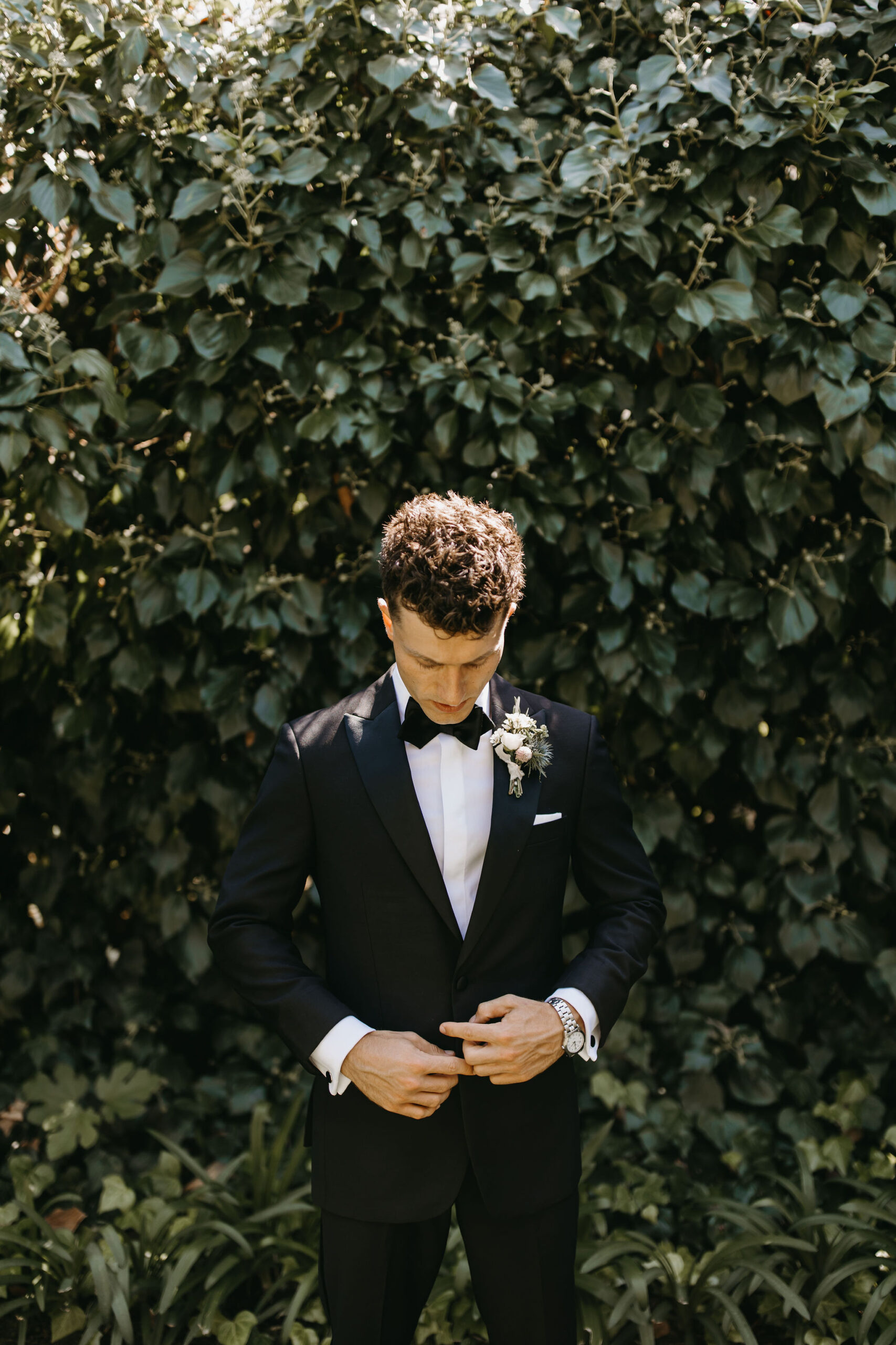 Groom standing outdoors in front of a green background | documentary style wedding photos