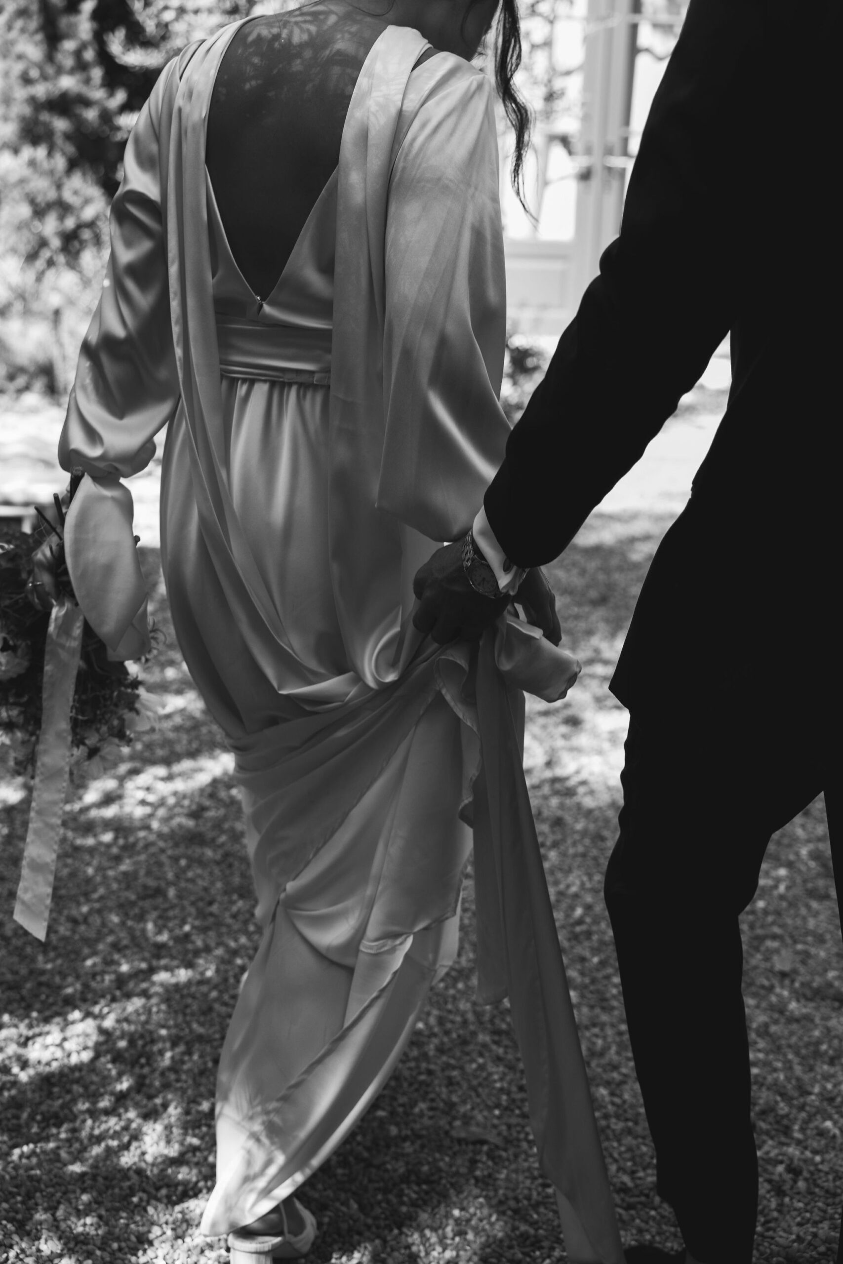 bride and groom walking together while groom holds brides dress