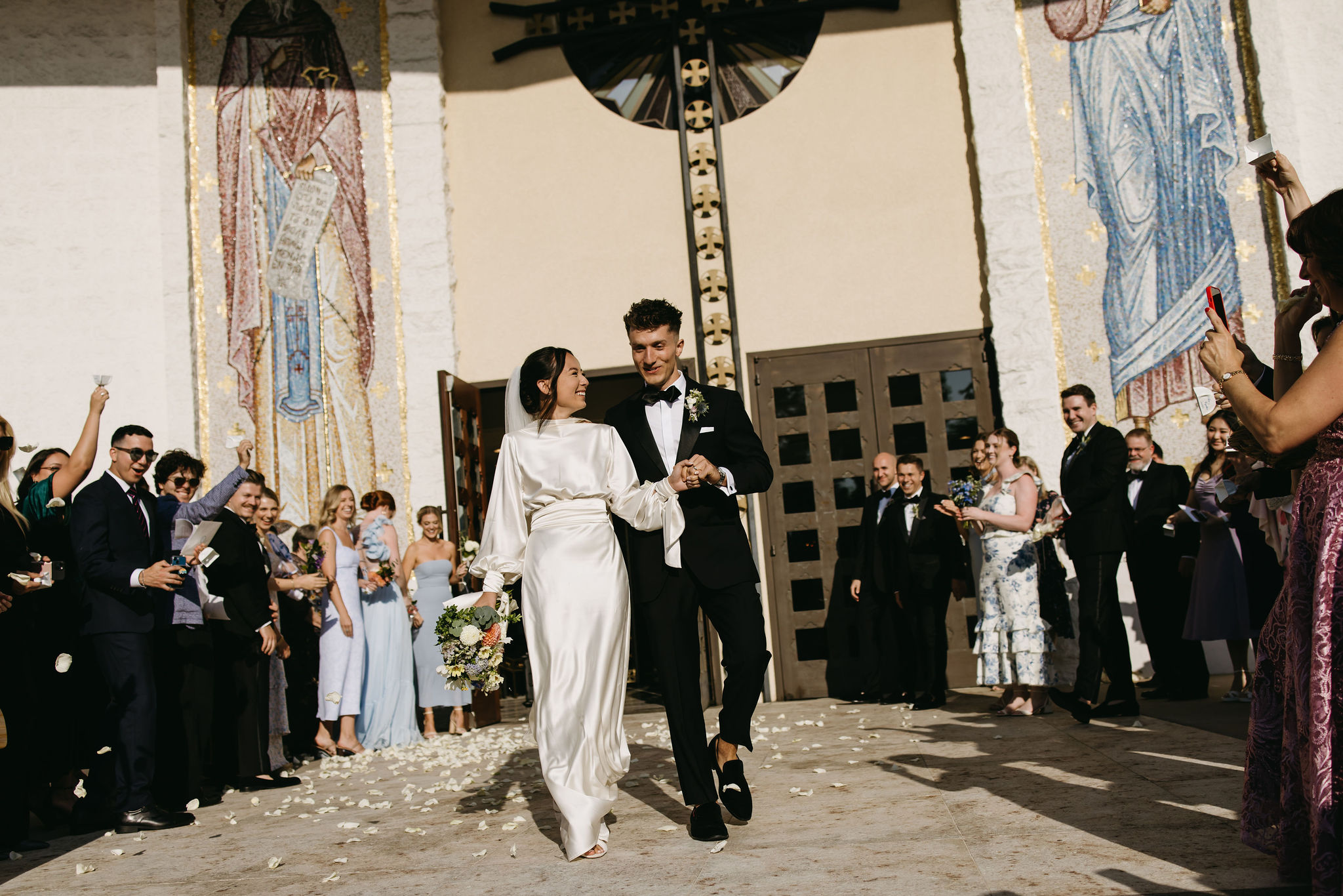 Bride and groom exiting their wedding ceremony while guests throw petals